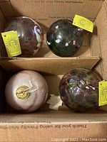 Four art glass balls in a cardboard box, three tagged Kitras Art Glass, showing various internal multicolor designs.
