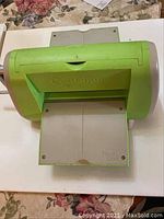 Top side view of the green Sizzix Cuttlebug embossing machine showing the handle and base platform with soiling.