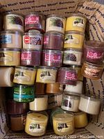 Top view of multiple small Bath and Body Works votive candles of varying scents like Fresh Balsam and Candied Sugar Plum, packed in a USPS box.