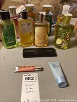 Overview of multiple Bath & Body Works shower gel bottles, Avon brow trimmer box, Estée Lauder lotion tube, and lip gloss on tabletop