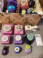 Photo showing box containing multiple craft punches with different shapes and colors arranged outside and inside the box