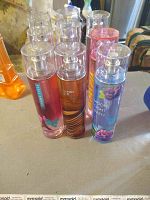 Photo showing several Bath & Body Works body spray bottles, including Paris Amore, Vanilla Sugar, and Moonlight Path, arranged on a table surface.