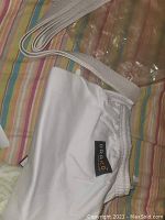 Photo showing white pants with elastic waistband and visible 'Draio' label, along with a white woven belt placed on a striped surface.
