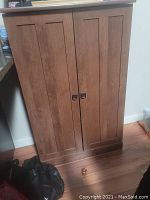 Front view of the closed wooden DVD cabinet showing paneled doors and missing handle hardware.