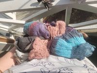 Photo showing a handful of scarves in various colors and textures including knitted pink, crinkled blue, and smooth gray scarves piled together.