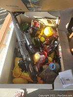 Box filled with assorted toy vehicles, a Nerf gun, and a yellow smiley foam ball.
