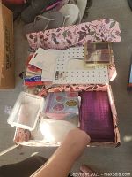 Floral box containing assorted drawing tools including stencils, pencil sharpener, plastic container, and craft items.