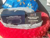 Boxed Mobile Phone Virtual Reality Headset and MP3 Digital Music Player with FM Radio packaging shown side by side on a red plush surface.