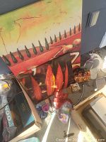 Photo showing canvas paintings with sunburst and chili pepper designs, along with various decorative objects on the ground.