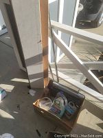 Tall wooden shelves leaning against wall outdoors with basket of cleaning supplies and several DVD cases inside basket.