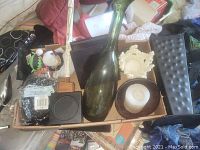 Photo showing tall green decorative bottle, coasters, ivory candle holder with candle, black tray, and cream ceramic candle holder on top, black shredded decorative paper in package, and a wooden mallet-like object.