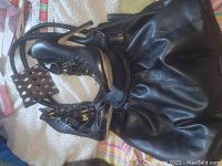 Photo showing pair of black high heels with two black bags, wooden photo holder, and small ornament on bedspread.