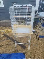 White metal bird cage on stand, showing full height and base