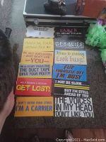 Photo of multiple brand new bumper stickers arranged in rows on the floor, showing various humorous and sarcastic text designs with colorful backgrounds and fonts.