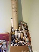 Box with many rolled posters and tubes, one tube labeled 'Royal Canadian Poster Series'