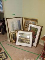 Cluster of seven framed artworks leaning against wall
