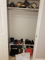 Closet with shoes and boots on racks at bottom, various handbags and bags on the floor, hats on top shelf.