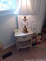 Side table with glass top holding the lamp, next to window and door with books in background