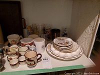 Shelf containing assorted cups, mugs, collectible glasses, and plates with gold detailing