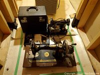 Two machines on floor: front hand-crank and rear electric, plus carrying case and accessories tray