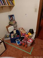 Various toys and books on floor, including blue bin and white carrying case