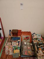 Overview of collectible cards and matchbooks arranged on the floor including albums, tins, and boxes
