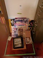 Overview showing stacked framed photos and prints leaning against wall, pennant flags sheet, Stanley Cup poster, and box of coins
