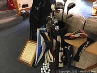 Photo showing golf bag filled with assorted golf clubs, umbrella, framed golf rules, and golf balls at the base