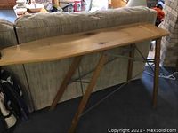 Side view showing the full length and wooden surface of the vintage ironing board with metal folding legs and some water stains.