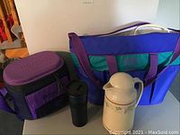 Two insulated cooler bags in purple and blue, a black thermos, and a vintage-style carafe with travel mug lid.