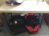 View of the folding table from the front showing the white resin tabletop and black metal legs underneath along with some bags placed beneath the table.
