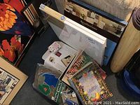 Photo showing decorative painting book, moss, glue tool, canvas boards, quilting and stencil books packed together on the floor.
