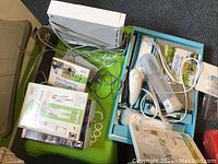 White Nintendo Wii console with cables, two Wii controllers, joystick controller, and boxed fitness games with covers.