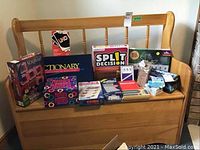 Maple wood storage bench with spindled backrest shown from front angle with various boxes of games and items on top (not included). Shows condition and design of the bench.