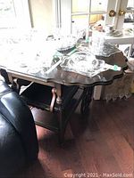 Wood tea cart from an angled view showing drop down leaves, top surface, and part of handle with various glassware on top.