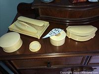 Vintage dresser set items arranged on wooden surface. Shows three celluloid containers, the tray with clothing brush, and button hookers and nail buffer placed on the tray.