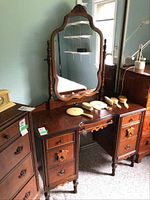 Full view of wood dressing table showing the large rotating mirror, 7 drawers, and surface with scratches. Temporary display items on top are not part of the lot.