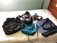 Photo showing all bags grouped on bed including the suede backpack, black bag, small brown pouch, teal handbag, and polka dot tote bag.