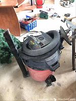 Craftsman red and black wet/dry vacuum cleaner with hose coiled on top, placed in garage environment.