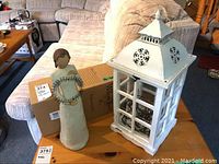 Photo showing both the white and tin lantern and the Willow Tree figurine on a wooden table with packaging boxes in background.