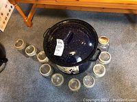 Top view of the blue speckled enamel canning pot surrounded by 10 glass jars with metal lids on a carpeted floor.