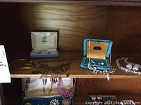 Wide view of all jewelry items displayed on wooden shelf including necklaces, bracelets, and earrings in boxes