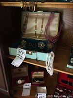Open jewelry box showing multiple colorful beaded necklaces, brooches, earrings, pins arranged inside on blue lining