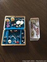Overall view of the blue velvet box with assorted clip-on earrings and grey plastic container with vintage hair pins