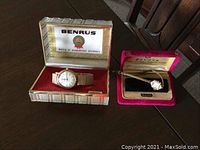 Both watches in their original boxes on a dark wood table, the Benrus watch in a light-colored box with red velvet interior and the Bulova watch in a pink velvet box.