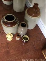 Overview of all ceramic crocks, jars, vases, and pots arranged on wooden floor, showing variety of shapes and finishes.