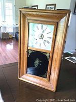 Front view of vintage wooden framed wall clock with Roman numeral dial and lower decorated glass panel