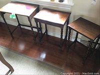 Three wooden stacking tables shown side by side against wall on hardwood floor, all with turned legs and rectangular tops