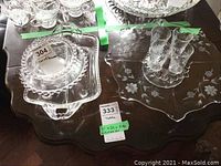 Clear etched glass serving pieces on a wooden table including dessert and serving trays, four liquor glasses, and a small bowl