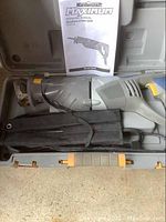 Reciprocating saw in plastic case with operating manual and black accessory pouch inside case.